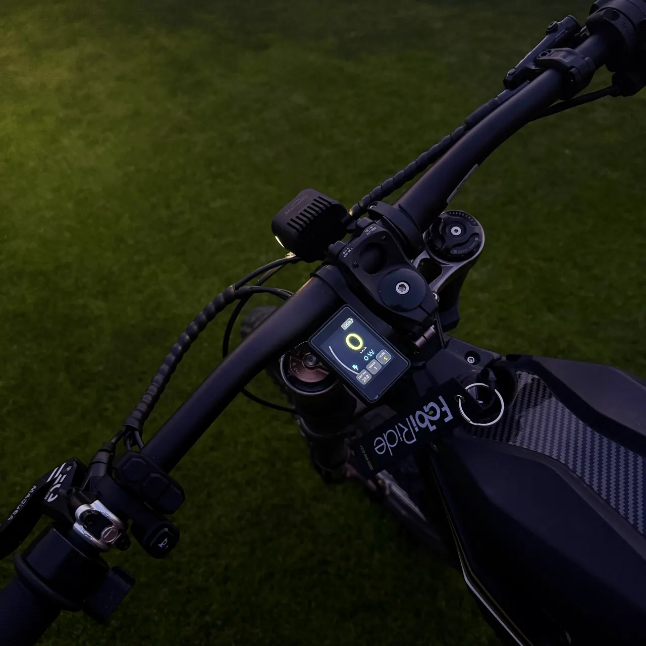 Dash Pro, pritvirtintas ant kalnų dviračio vairo sutemus, jo spalvotas ekranas - vienintelė šviesa kadre, rodo 100% bateriją, S režimą ir 27,2 km kelionę.